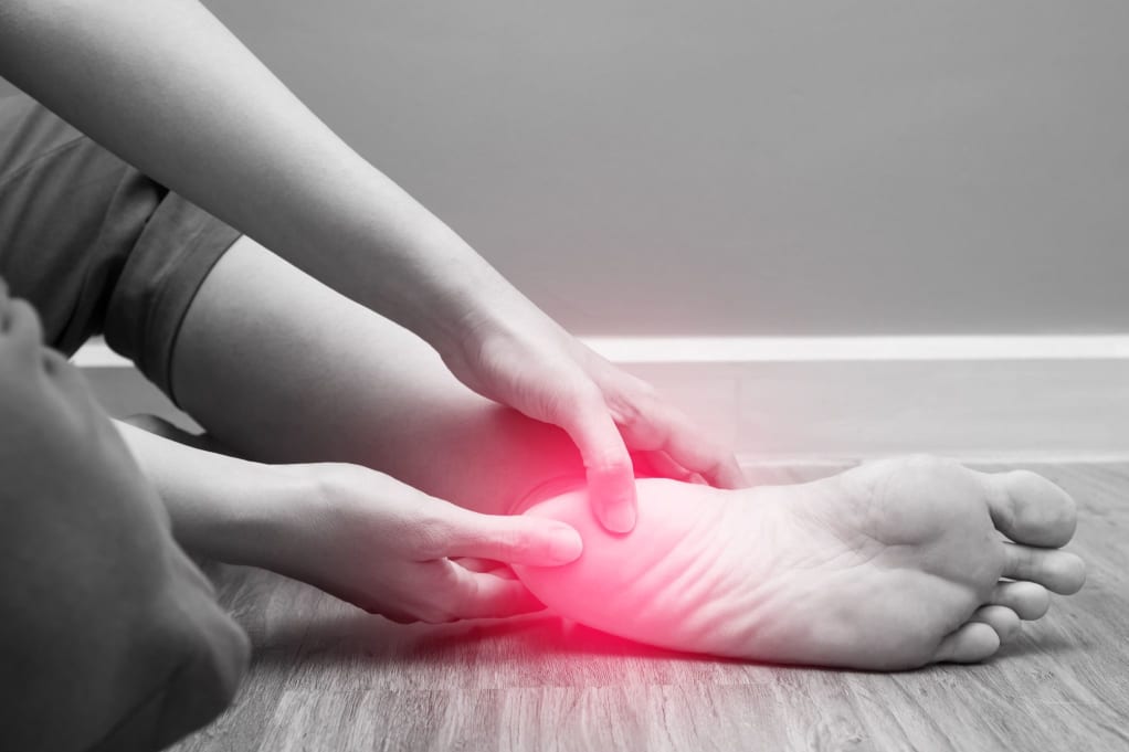 A person touching their foot indicating discomfort from plantar fasciitis