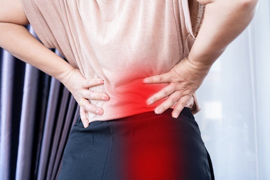 A person holding her back in pain from either degenerative disc disease or sciatica
