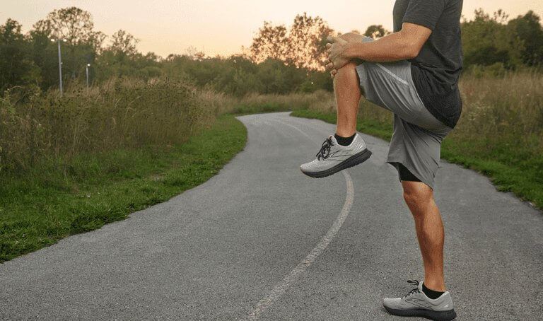 Man stretches leg roadside, highlighting knee pain treatment at Forte Sports Medicine