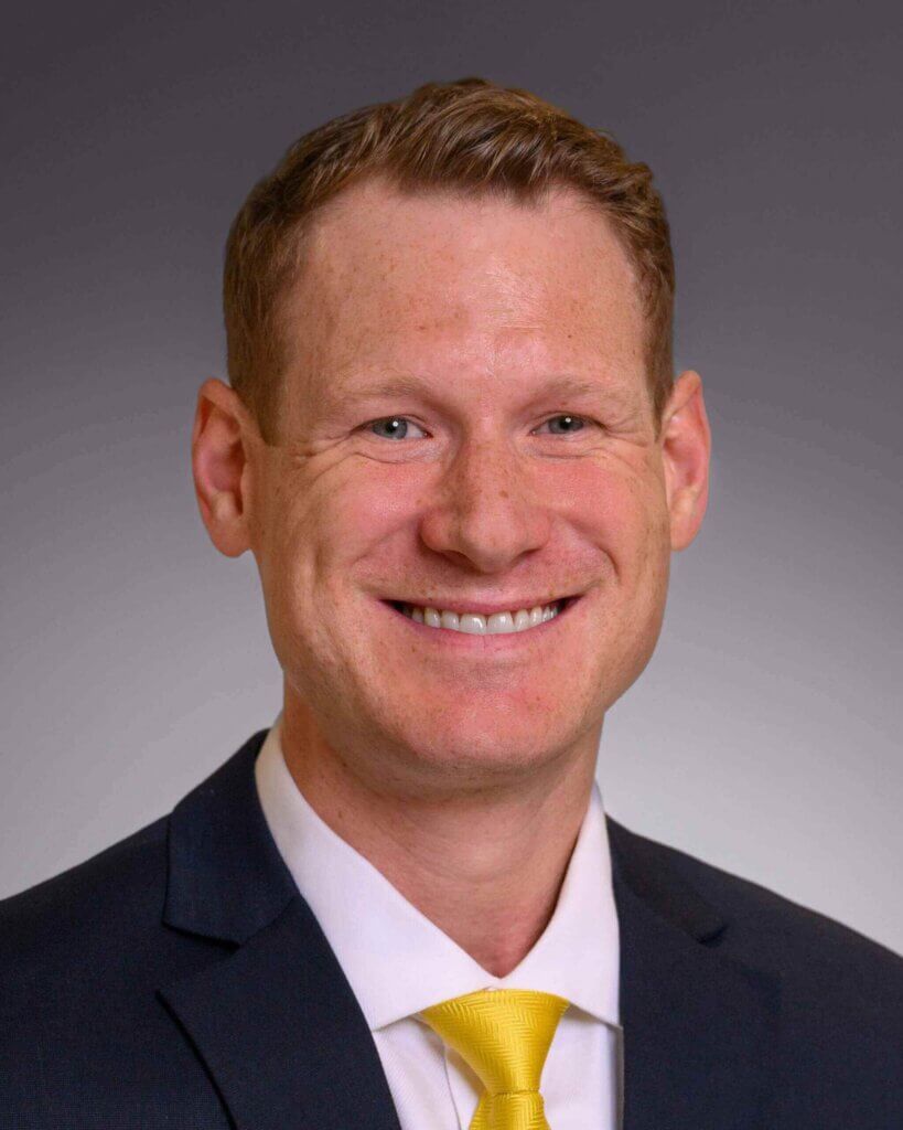 Ryan Nixon, Orthopedic Surgeon at Forte Sports Medicine, smiles in a suit with a yellow tie