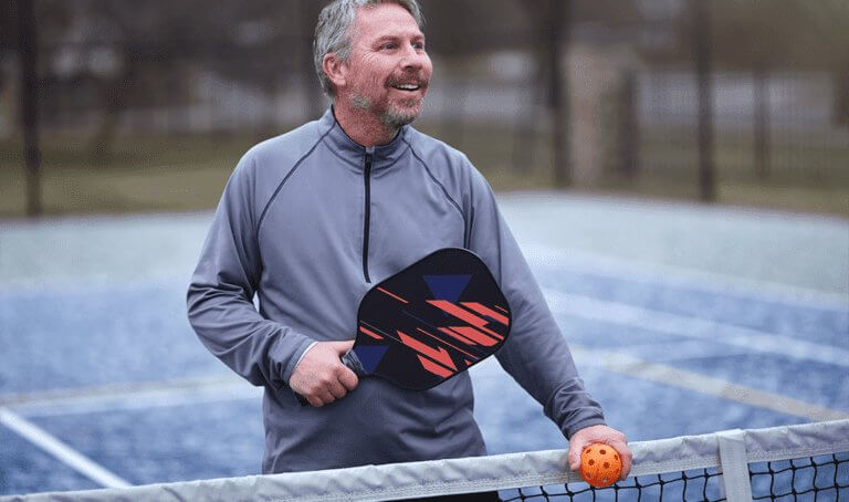 Smiling man with tennis racket promoting wrist pain orthopedic care at Forte Sports Medicine