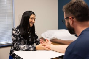 A woman at a desk with a man holding her hand, discussing Trigger Finger at Forte Sports Medicine